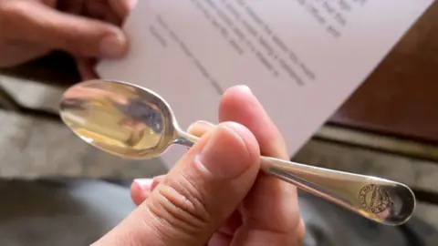 BBC A silver teaspoon is held between finger and thumb